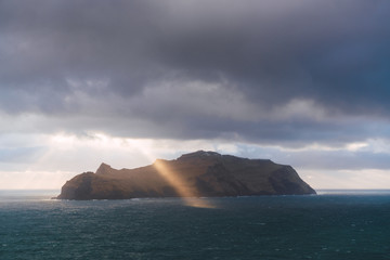 Sun shining through clouds near cliff