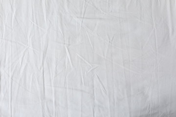 White fabric texture background. Wrinkled, crumpled fabric. Top view of unmade bed sheet after night sleep. Soft focus