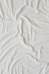 White fabric texture background. Wrinkled, crumpled fabric. Top view of unmade bed sheet after night sleep. Soft focus