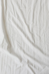 Fototapeta na wymiar White fabric texture background. Wrinkled, crumpled fabric. Top view of unmade bed sheet after night sleep. Soft focus
