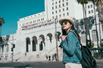 Obraz premium vintage style photo young stylish girl tourist in sunglasses carry bag walking in urban on street looking around sightseeing with blue sky. Los Angeles city hall on sunny day California in background
