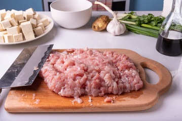 Minced meat and traditional Chinese knife Tsai Dao on a cutting board and ingredients for cooking Mapo doufu.