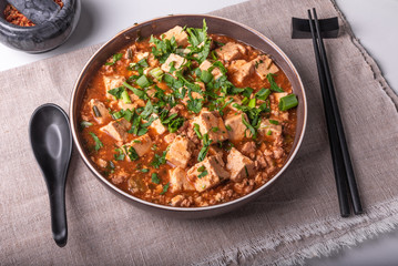 Traditional Chinese dish Mapo tofu with minced meat and tofu cheese in a bowl on a linen rustic napkin