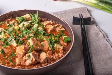 Traditional Chinese dish Mapo tofu with minced meat and tofu cheese in a bowl on a linen rustic napkin