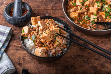 Popular Chinese Sichuan dish - a bowl of rice with spicy mapo tofu and a plate of mapo doufu on a rustic wooden table