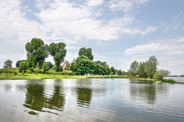 Fototapeta na wymiar Trees and bushes reflecting in the water of the river Waal near Woudrichem, The Netherlands, with historic Loevestein castle visible in the background