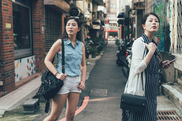 two young asian girl tourists consulting right way in city using smartphone gps in street searching...
