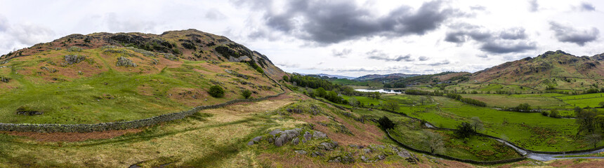 Fototapeta na wymiar Aerial over the lake district with mountains and hills and dramatic sky, England panoramic