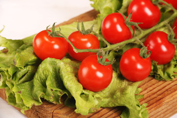 Ripe fresh Juicy organic brunch of cherry tomatoes on cutting board with Green Lettuce on a white table