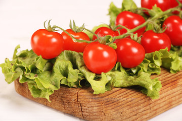 Ripe fresh Juicy organic brunch of cherry tomatoes on cutting board with Green Lettuce on a white table