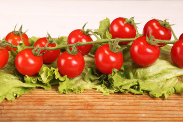 Ripe fresh Juicy organic brunch of cherry tomatoes on cutting board with Green Lettuce on a white table