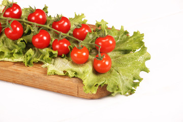 Ripe fresh Juicy organic brunch of cherry tomatoes on cutting board with Green Lettuce on a white table