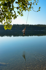 Obraz na płótnie Canvas man swinging on a rope swing into a lake in canada