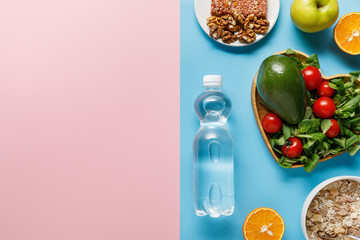 top view of bottle with water and diet food on blue and pink background