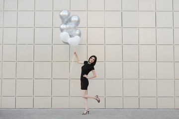 Beautiful young woman in a black dress with  balloons in summer oudoor