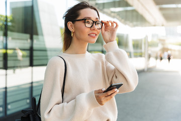 Photo of brunette caucasian woman using cellphone while walking in big city street