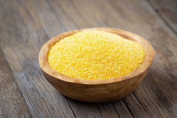Wooden bowl with raw polenta on wooden table.