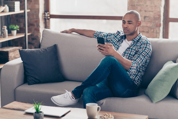 Portrait of concentrate gorgeous man hold hand modern technology device social media smm dressed denim shirt jeans checked plaid sit divan room apartment