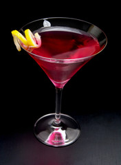 Pink cosmopolitan drink with lemon peel on black