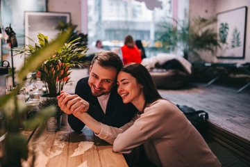 Happy loving guy holds his girlfriend's hand sitting at the table in the cafe and looks at her.