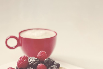 red cup with coffee and wild berries raspberries, blackberries and blueberries in vintage style with texture, copy space,