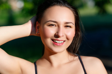 close up portrait of a young beautiful smiling happy brunette girl in outdoor Park on a Sunny summer day correcting hand loose hair