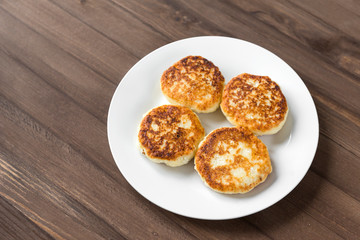 4 pancakes on a white plate on a wooden background, cheesecakes, cottage cheese pancakes