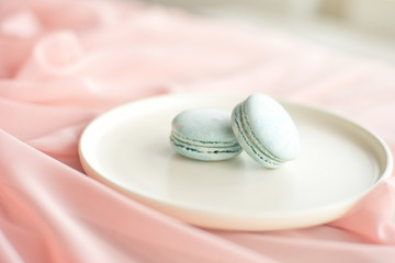Blue macaroni or macaroon cakes with pink textile flowers on a white ceramic plate on a gray wooden background. Flat lay, top view, copy space