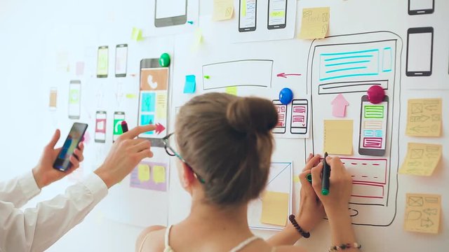 Designers is developing a web application for mobile phones. Woman draws a mockup of interface to smartphone. User experience. 