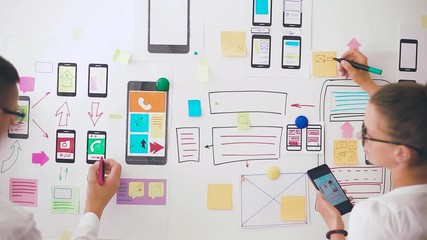 Designers is developing a web application for mobile phones. Woman draws a mockup of interface to smartphone. User experience. 