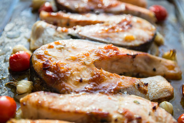 Grilled salmon steak with addition of lemon, rosemary, garlic, onion and spices on grill plate, top view. Grilled fish, seafood