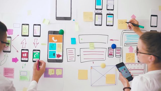 Designers is developing a web application for mobile phones. Woman draws a mockup of interface to smartphone. User experience. 