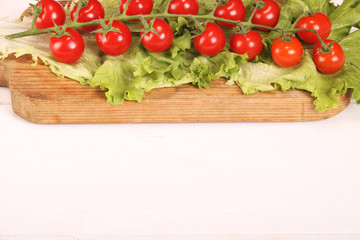 Ripe fresh Juicy organic brunch of cherry tomatoes on cutting board with Green Lettuce on a white table. Copy space