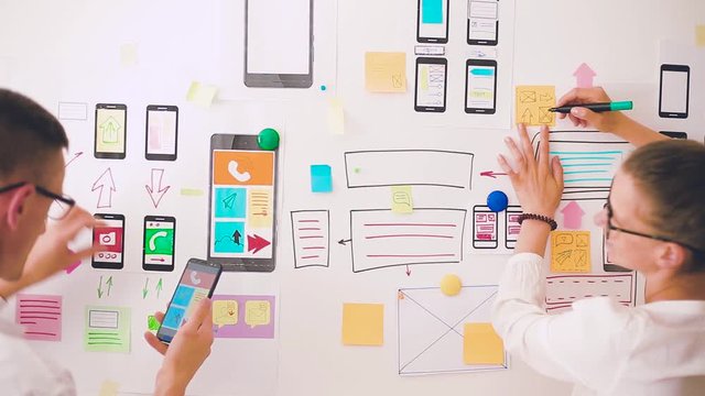 Designers is developing a web application for mobile phones. Woman draws a mockup of interface to smartphone. User experience. 