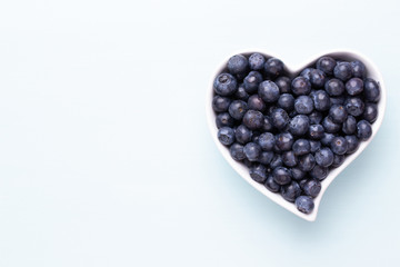 Fresh blueberries, in a heart shaped bowl on a wooden background.