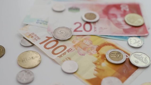 Different Israeli shekel coins and bills spread on white background