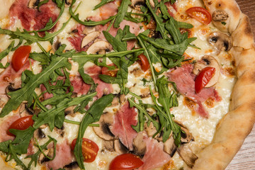 top view macro of pizza with arugula, ham, mushrooms and tomatoes