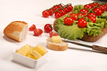 Ripe fresh Juicy organic brunch of cherry tomatoes on cutting board with Green Lettuce, bread, butter on a white table