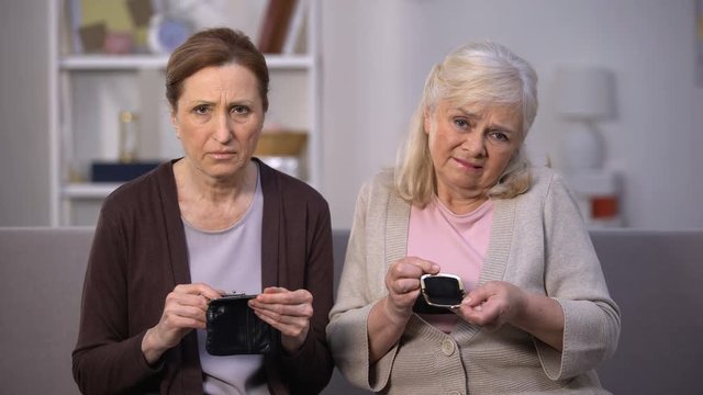Sad senior female friends looking in empty wallets, poor budget, low incomes