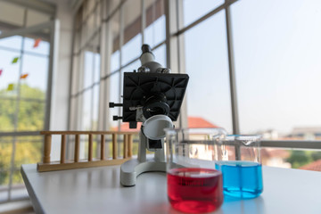 The scientific microscope  for testing with the laboratory glassware on the white table.