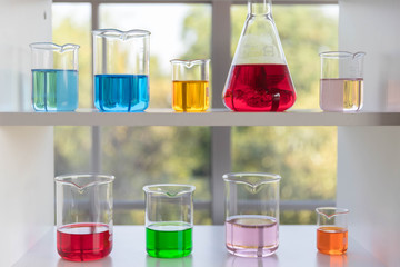 The different size of laboratory glassware on the white shelf.