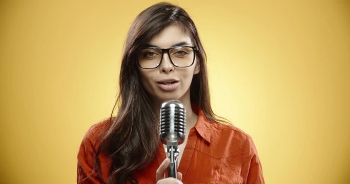 Cheerful asian girl in casual clothes singing into microphone dreaming of becoming a famous singer, isolated over yellow background close up 4k