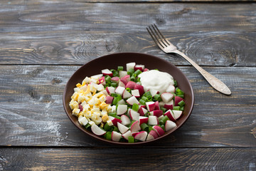Fresh radish salad with green onions, boiled egg and sour cream on a wooden background, rustic style. Delicious homemade food