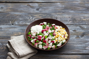 Fresh radish salad with green onions, boiled egg and sour cream on a wooden background, rustic style. Delicious homemade food