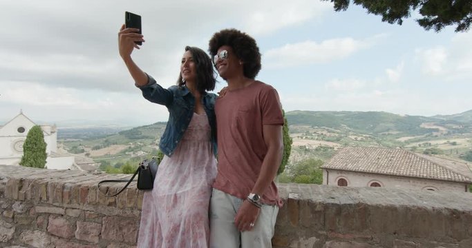 Romantic couple taking a selfie with smartphone in rural town of Assisi.approach wide shot.Friends italian trip in Umbria.4k slow motion
