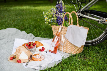 Beautiful summer picnic with strawberries, cheese and rose wine on the lawn in the city park