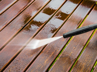 Close up view of using pressure washer to clean impregnated wood terrace outdoors in the spring.