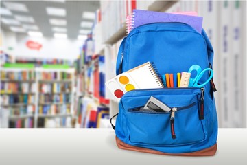 Open blue school backpack on a wooden desk and bokeh background.