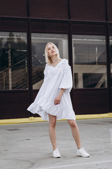 The girl is dressed in a stylish white, lush summer dress, dynamically poses for the photo, posing against street , urban clothing style. Street photography