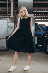 Stylish young girl dressed in a comfortable, daily black dress and white sneakers pose for a photo on an industrial background, urban clothing style. Street photography